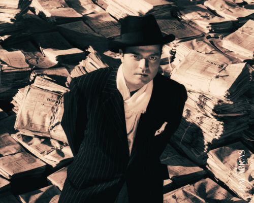 Fotograma de la película Ciudadano Kane con el protagonista en primer plano sobre una montaña de periódicos - Cómo escribir un folleto - Magníficas Palabras Copywriting